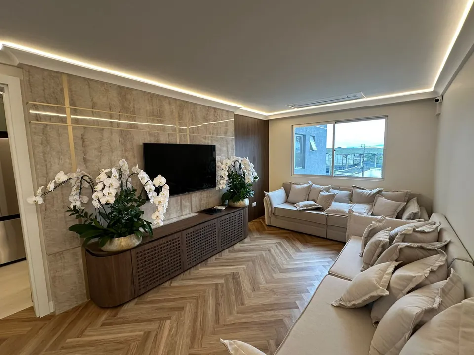 Sala de estar com painel de TV, sanca iluminada e piso em espinha